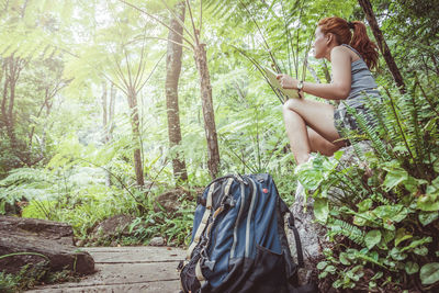 Low angle view of woman holding book sitting on rock in forest