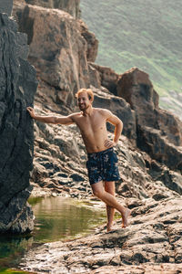 Full length of shirtless man standing on rock at beach