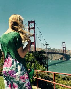 Rear view of woman standing by bridge against sky