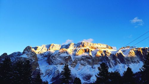 Low angle view of snowcapped mountains against clear blue sky