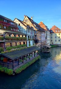 View of buildings by river against blue sky