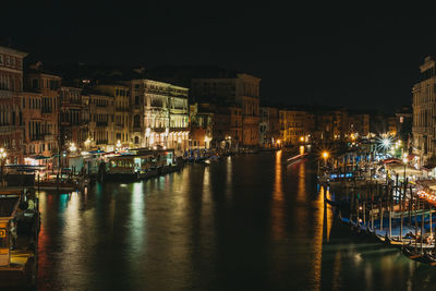 Boats moored in river against illuminated buildings in city at night