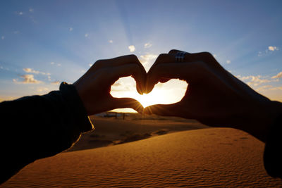 Midsection of man making heart shape against sky during sunset