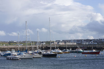 Sailboats moored on harbor against sky