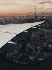 Cropped image of airplane wing over cityscape seen through window during sunset