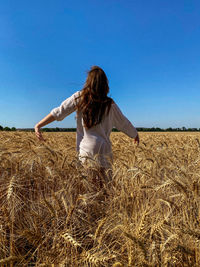 Rear view of woman standing on field against clear blue sky