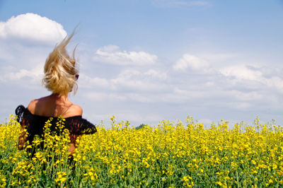 Rear view of young woman standing on oilseed rape field