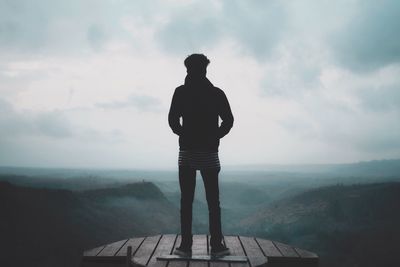 Rear view of man standing on mountain against sky