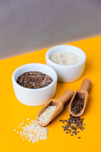 Wooden spoons with sesame and flax seeds lies in a white mortar on a yellow background. healthy eat