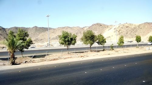 Road by trees against clear blue sky