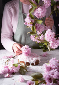 A woman decorates a homemade easter cake with pink sakura flowers,spring blossom