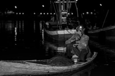 Mature man smoking while sitting on boat in river at night
