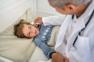 Doctor examining boy in bed at home