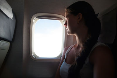 Young woman looking through window while sitting in airplane