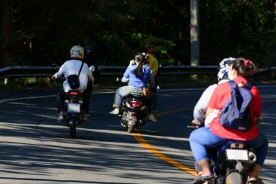 Rear view of people riding motorcycle on road