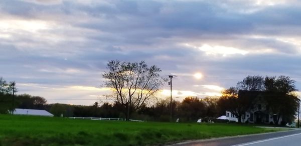 Road by trees on field against sky at sunset