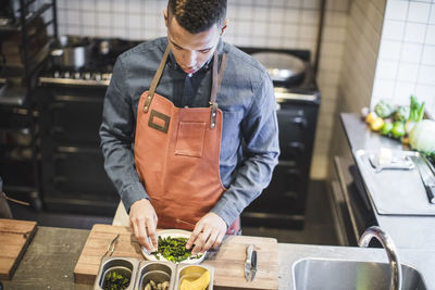 High angle view of young chef preparing food in plate at kitchen counter in restaurant