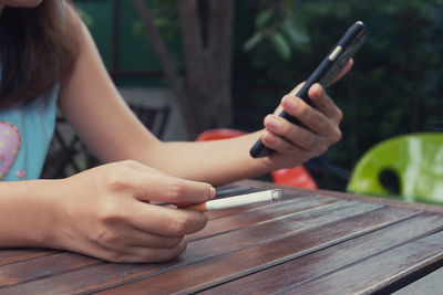 Midsection of woman with cigarette using mobile phone at table