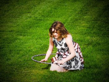High angle view of girl kneeling by plastic hoop on grassy field