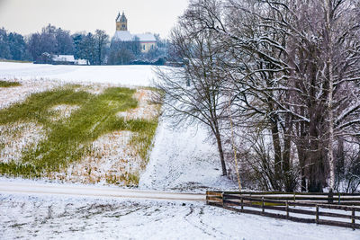 Snow covered road by trees on field during winter