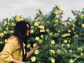 Side view of young woman against yellow flowering plants