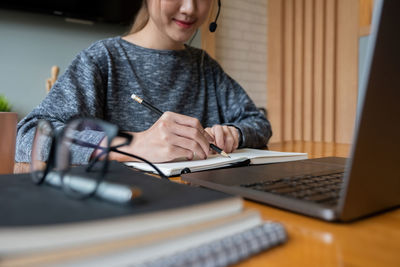 Midsection of woman using phone while sitting on table