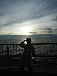 Woman standing by railing against sea during sunset