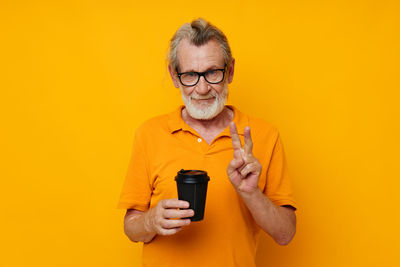 Portrait of senior man holding cup gesturing against yellow background