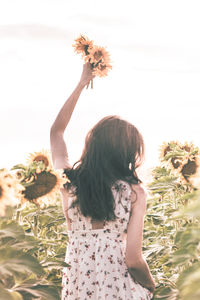 Woman standing by flowering plant on field against sky