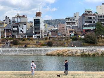 People by river in city against sky