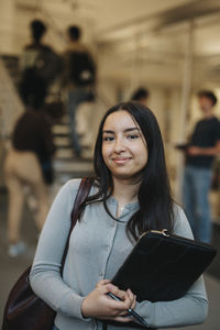 Portrait of confident female student carrying file folder standing in university