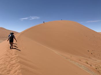 Scenic view of people walking in desert up large sand dune against clear blue sky