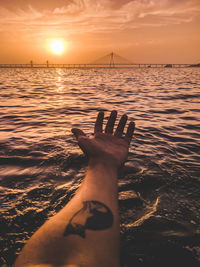 Cropped hand of man over sea against sky