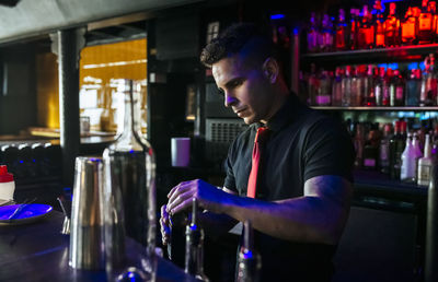 Male bartender holding alcohol bottle while standing in bar