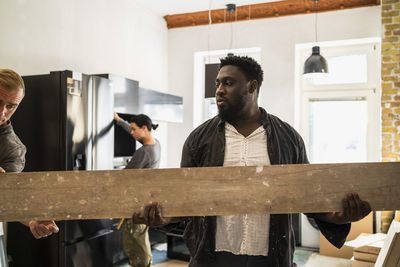 Multiracial male carpenters carrying plank while working in kitchen at apartment