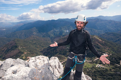 Concept: adventure. climber man with helmet and harness. in the top of the mountain. with open arms and smiling showing the landscape. via ferrata on rock.