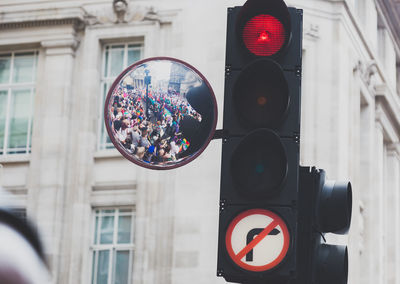 Reflection of crowd on mirror attached to stoplight against buildings in city