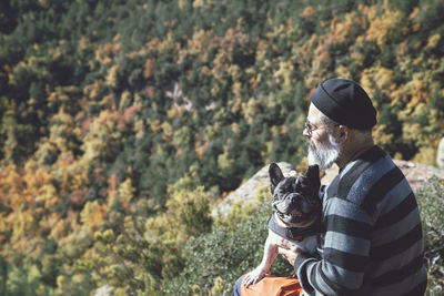 Man sitting with dog on rock looking at landscape on mountain cliff