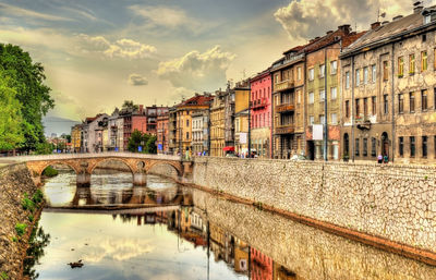 Bridge over canal by buildings in city against sky