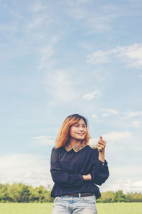 Smiling young woman with coffee cup standing against sky