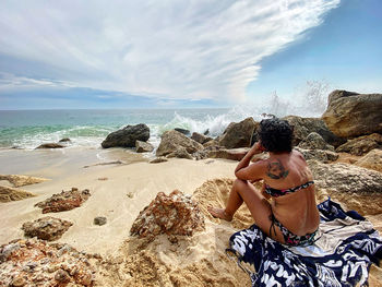 Woman sitting on rock at beach against sky