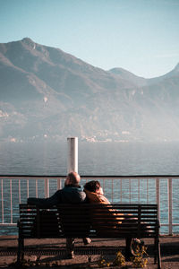Rear view of man sitting on bench against mountain range