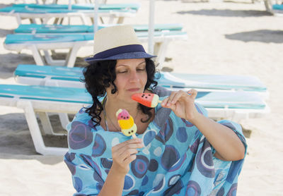 Beautiful young woman in blue dress holds colorful ice cream at the beach