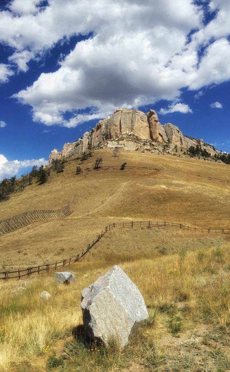 sky, landscape, tranquil scene, tranquility, mountain, scenics, nature, rock formation, beauty in nature, cloud - sky, grass, non-urban scene, rock - object, cloud, physical geography, remote, mountain range, geology, arid climate, blue