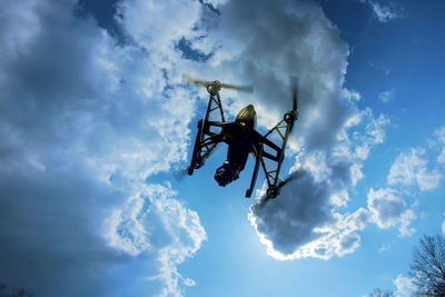 Low angle view of drone flying against cloudy sky