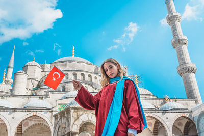 Low angle portrait of woman holding flag against mosque