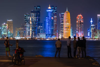 People on illuminated modern buildings in doha city at night