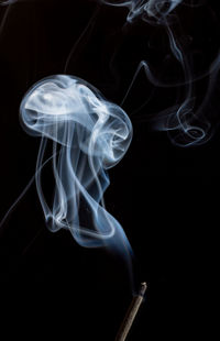 Close-up of smoke over incense against black background