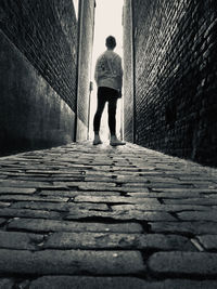 Rear view of man standing on footpath amidst wall