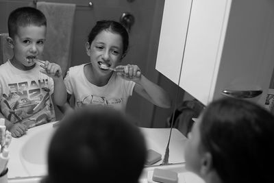 Reflection of siblings brushing teeth on mirror in bathroom